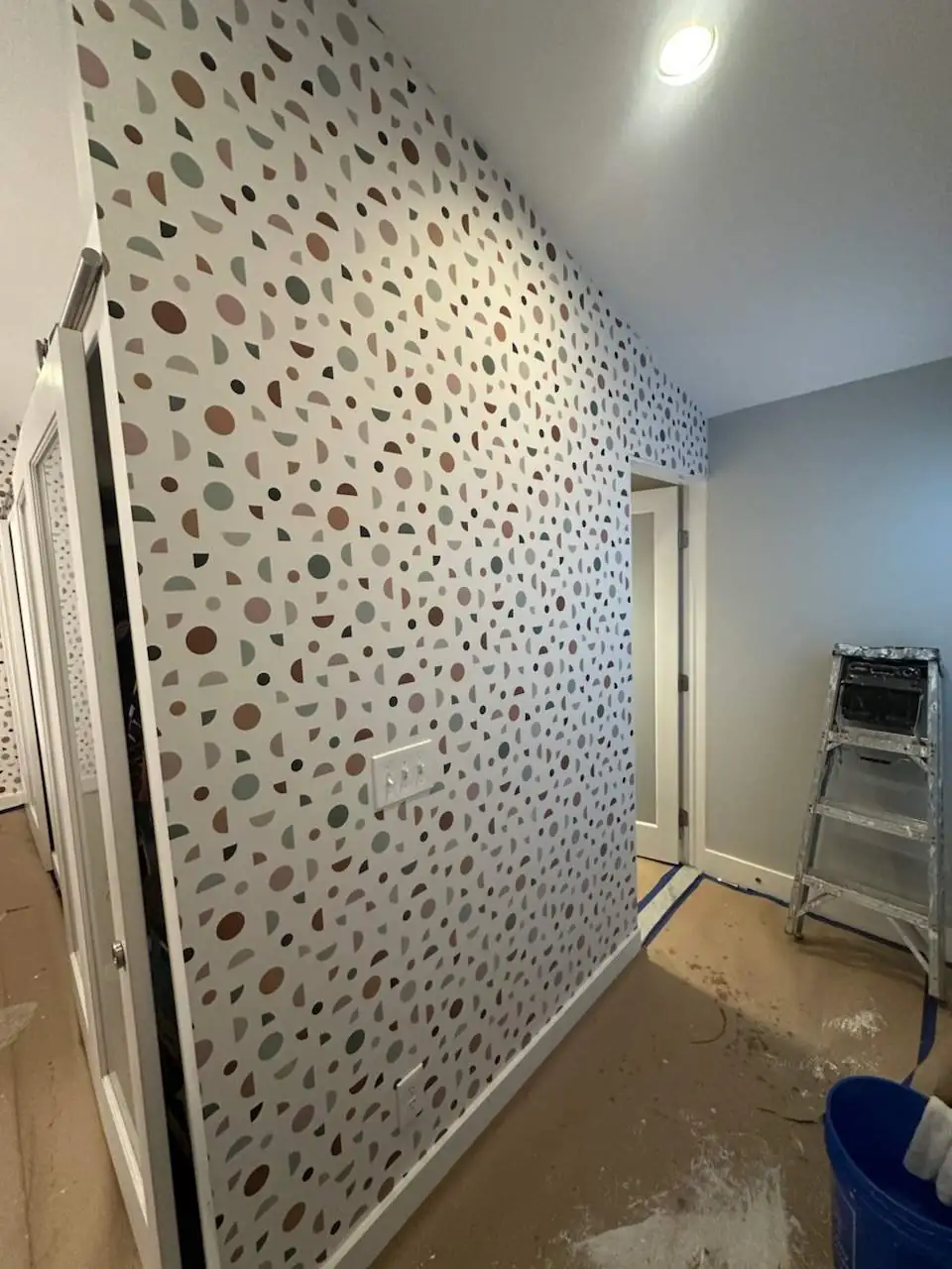 A speckled wallpaper hung along a hallway wall, with a ladder and drop cloths still in place
