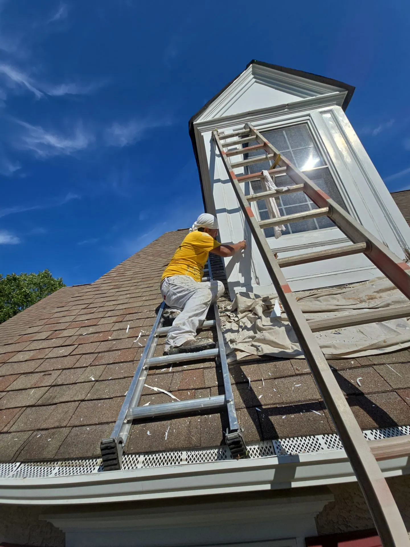 A painter on an extension ladder working at a second story roofline