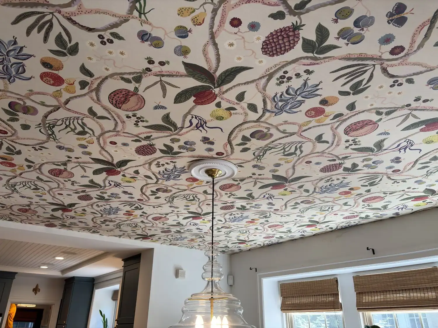 A dining room ceiling papered in a botanical fruit-and-vine pattern, fitted around a ceiling medallion and pendant light